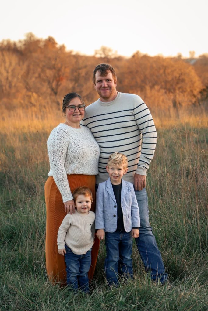 Ryan Helmuth and his wife and two sons stand in a field of tall green grass for a family portrait on an autumn afternoon